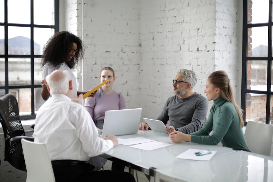 A team of diverse professionals discussing a project in a modern office setting with laptops and documents