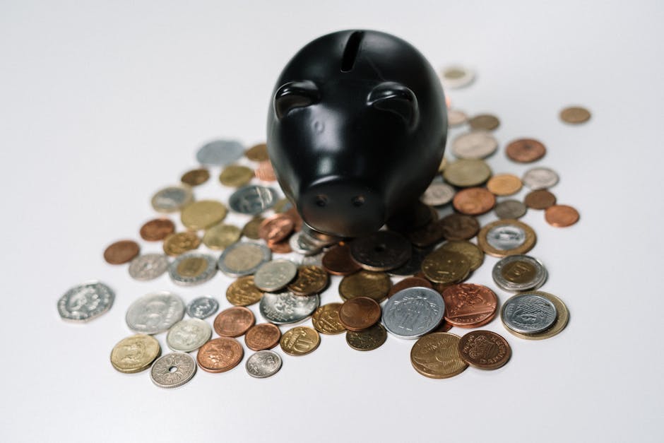 Black piggy bank surrounded by a variety of coins on a white surface, symbolizing savings and finance